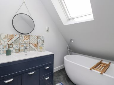 A bathroom with a freestanding bathtub under a skylight and a vanity unit with patterned tiles at Greystones in Upton St Leonards