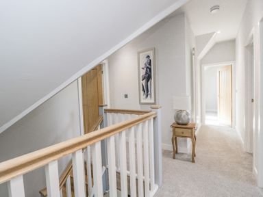 A carpeted hallway with a wooden side table and lamp a framed picture and wooden doors at Greystones in Upton St Leonards