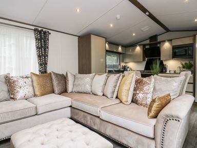 A living area with a beige sectional sofa and multiple decorative pillows next to a kitchen with cabinets and appliances at 43 Pony Meadow in Troutbeck Bridge