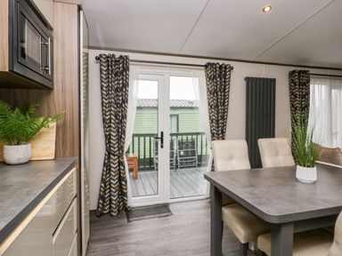 A dining area with a table and chairs next to sliding glass doors with patterned curtains at 43 Pony Meadow in Troutbeck Bridge