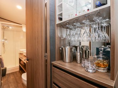 A bar area with hanging wine glasses metal ice bucket cocktail shakers and whiskey decanter next to a bathroom at 43 Pony Meadow in Troutbeck Bridge