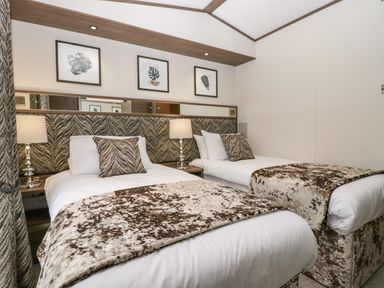 A bedroom with two single beds with patterned throws and pillows and lamps between the beds at 43 Pony Meadow in Troutbeck Bridge