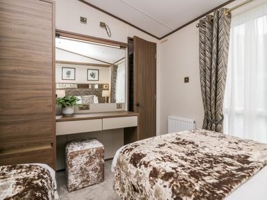 A bedroom with two beds a wooden wardrobe a dressing table with a plant and a cushioned stool at 43 Pony Meadow in Troutbeck Bridge
