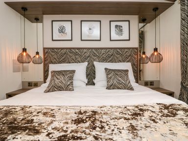 A bedroom with a double bed two pillows and cushions two hanging pendant lights and three framed pictures above the bed at 43 Pony Meadow in Troutbeck Bridge