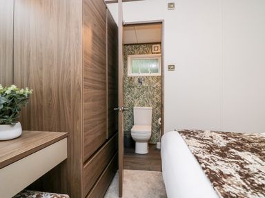 A bedroom with a wooden wardrobe a desk with a plant and a bathroom with a toilet visible through an open door at 43 Pony Meadow Troutbeck Bridge