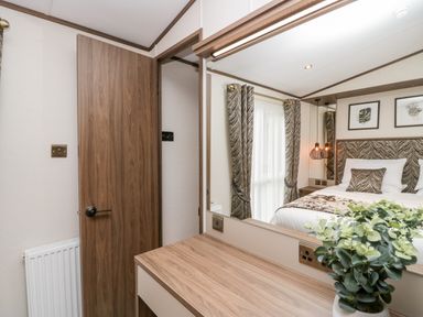 A bedroom with a wooden door a dressing table with a mirror and a potted plant and a bed with patterned cushions and curtains at 43 Pony Meadow in Troutbeck Bridge