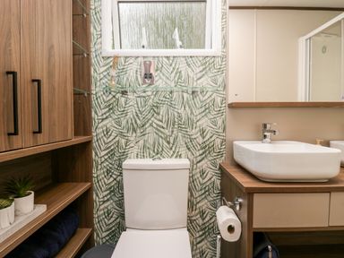 A bathroom with a toilet a sink wooden cabinets and green leaf patterned wall at 43 Pony Meadow in Troutbeck Bridge