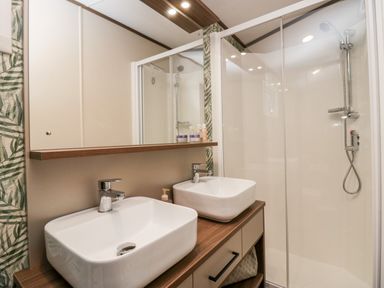 A bathroom with two white sinks on a wooden countertop and a glass shower enclosure at 43 Pony Meadow in Troutbeck Bridge