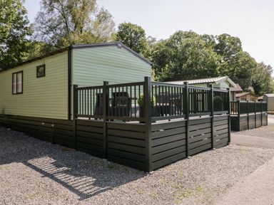 A mobile home with a fenced deck on a gravel lot with trees in the background at 43 Pony Meadow in Troutbeck Bridge