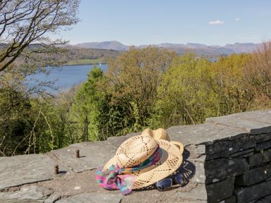 A stone wall with two straw hats and sunglasses with trees lake and mountains in the background at 43 Pony Meadow in Troutbeck Bridge
