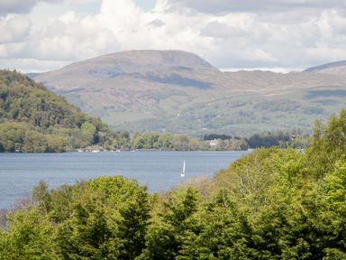 A lake with a sailboat surrounded by trees with hills in the background at 43 Pony Meadow in Troutbeck Bridge