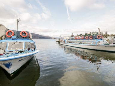 Two boats docked on a lake with hills and trees in the background at 43 Pony Meadow in Troutbeck Bridge