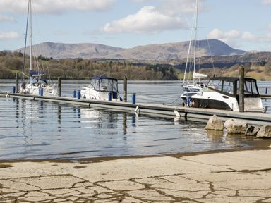 A dock with boats on a lake with mountains and trees in the background at 43 Pony Meadow in Troutbeck Bridge