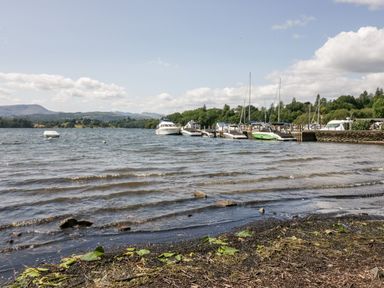 A lakeshore with boats docked at a pier and hills in the background at 43 Pony Meadow in Troutbeck Bridge
