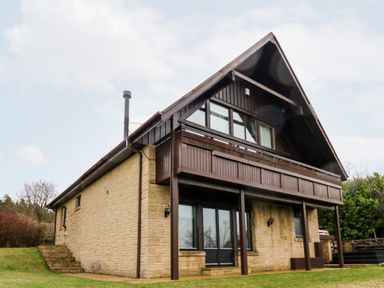 A two story house with stone lower walls and wooden upper walls with a balcony in a grassy area at Slaley Park Villa in Hexham