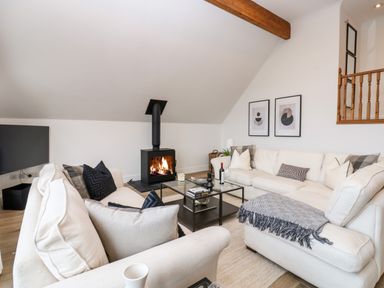 A living room with white sofas black cushions a wood burning stove and glass coffee table at Slaley Park Villa in Hexham