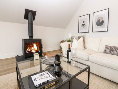 A living room with a fireplace a glass coffee table books a bottle of wine and a white sofa with cushions at Slaley Park Villa in Hexham