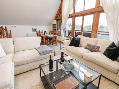 A living room with beige sofas glass coffee table wooden dining table and large windows at Slaley Park Villa in Hexham