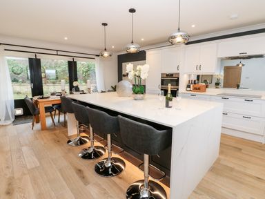 A kitchen with a large white island with five black bar stools and a dining table near glass doors at Slaley Park Villa in Hexham