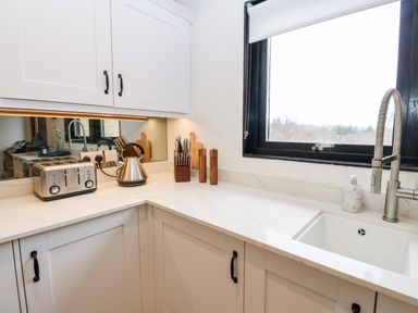 A kitchen countertop with a toaster kettle knife set and salt and pepper shakers near a window and sink at Slaley Park Villa in Hexham