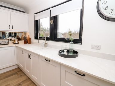 A kitchen with white cabinets a sink a black tray with glass bottles on the counter and a window above the sink at Slaley Park Villa in Hexham