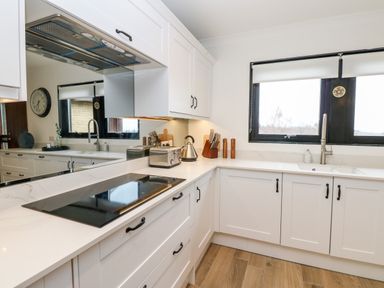 A white kitchen with black handles a stovetop a toaster kettle knife set and two windows at Slaley Park Villa in Hexham