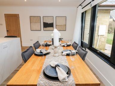 A dining table set with plates glassware and napkins in a room with a wooden door three abstract paintings and large windows at Slaley Park Villa in Hexham