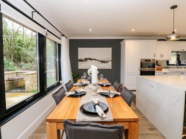 A dining table set with plates napkins and wine glasses next to large windows in a kitchen at Slaley Park Villa Hexham