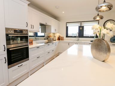 A kitchen with white cabinets a double oven a sink under a window and a countertop with a decorative vase at Slaley Park Villa in Hexham