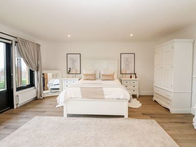 A bedroom with a bed two nightstands a wardrobe a mirror and curtains at Slaley Park Villa in Hexham