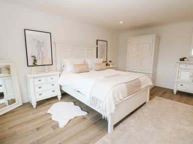 A bedroom with a white bed wooden furniture a mirror and framed line art at Slaley Park Villa in Hexham