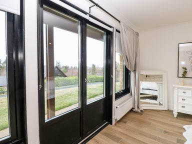 A room with black-framed glass doors and windows a white radiator beige curtains a white mirror leaning against the wall and a white dresser with drawers at Slaley Park Villa in Hexham