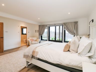 A bedroom with a bed white bedding pillows an armchair near window with curtains and an ensuite bathroom at Slaley Park Villa in Hexham