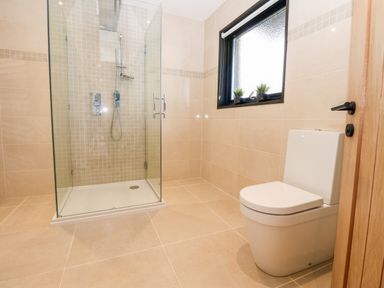 A bathroom with a glass shower enclosure a toilet and a window with two small plants on the sill at Slaley Park Villa in Hexham