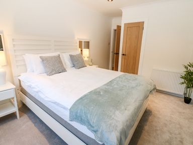 A bedroom with a white bed frame white bedding gray pillows a blue throw blanket two bedside tables with lamps wooden doors a radiator and a potted plant at Slaley Park Villa Hexham