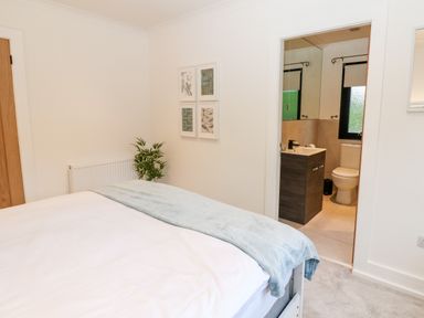 A bedroom with a bed a plant on the floor and an ensuite bathroom at Slaley Park Villa Hexham