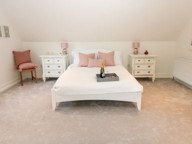 A bedroom with a white bed and pink pillows beside two white nightstands with lamps and a chair with pink cushions at Slaley Park Villa in Hexham