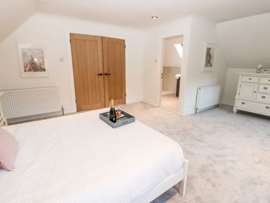 A bedroom with a white bed with a tray holding a bottle and glasses a wooden double door a white dresser and an open door leading to a bathroom at Slaley Park Villa in Hexham