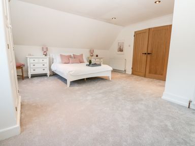 A bedroom with a white bed and pink pillows two white bedside tables with lamps and wooden double doors at Slaley Park Villa in Hexham