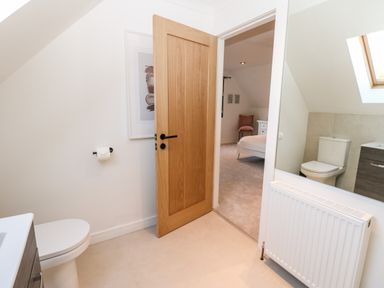 A bathroom with a toilet a wooden door a radiator and a mirror showing a bedroom at Slaley Park Villa in Hexham