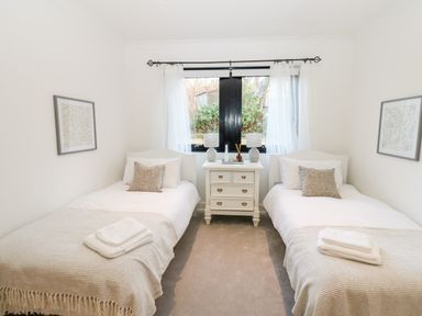 A bedroom with two single beds a white nightstand between the beds and a window at Slaley Park Villa in Hexham