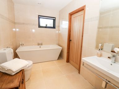 A bathroom with a bathtub a toilet a sink a wooden door and a small window at Slaley Park Villa in Hexham