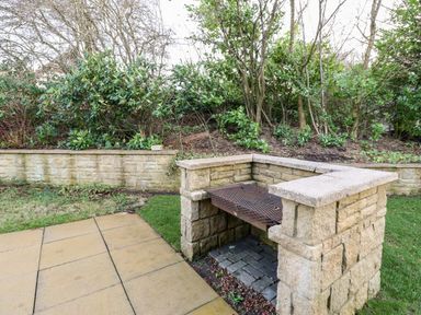 A stone outdoor barbecue grill area with a metal grate and surrounding greenery at Slaley Park Villa in Hexham