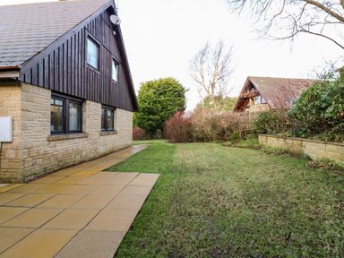 An exterior view of a house with a tiled pathway and grassy yard beside bushes and trees at Slaley Park Villa in Hexham
