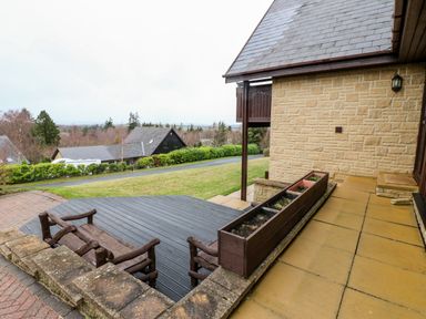 An outdoor patio area with wooden benches and planter boxes attached to a stone house at Slaley Park Villa Hexham