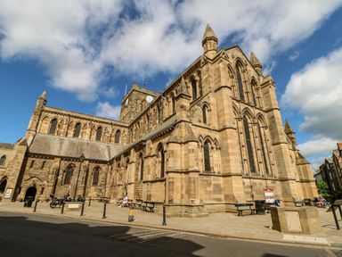 A large stone church with arched windows and benches outside under a partly cloudy sky