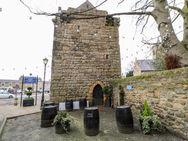 An outdoor area with wooden barrels, potted plants, stone walls, and a stone building at Slaley Park Villa in Hexham