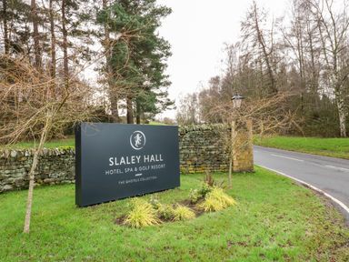 A sign for Slaley Hall hotel spa and golf resort on a grassy roadside with trees and stone wall in the background at Slaley Park Villa in Hexham