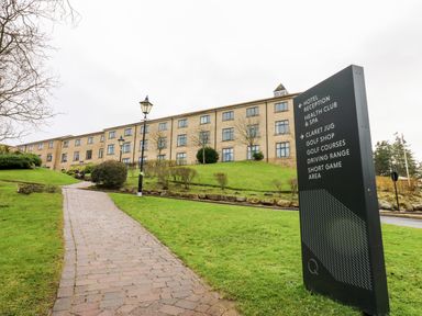 A pathway leading to a large building with windows and a sign showing directions to hotel reception health club spa and golf facilities at Slaley Park Villa in Hexham