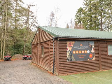 An outdoor wooden building with a green metal roof and an Allout Adventures sign on the side with quad bikes parked nearby at Slaley Park Villa in Hexham